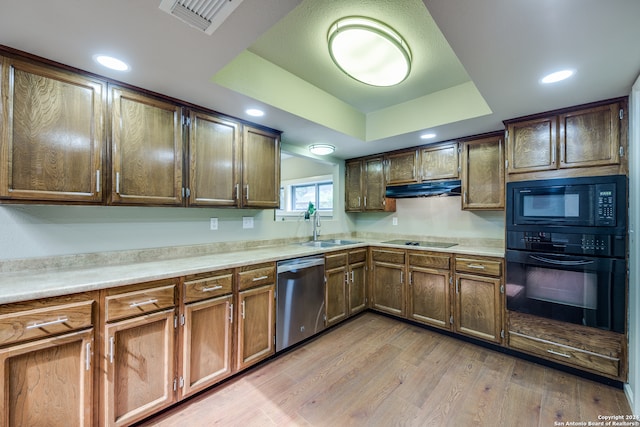 kitchen featuring black appliances, light hardwood / wood-style flooring, a raised ceiling, and sink