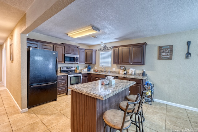 kitchen with dark brown cabinetry, appliances with stainless steel finishes, a center island, sink, and light tile patterned floors