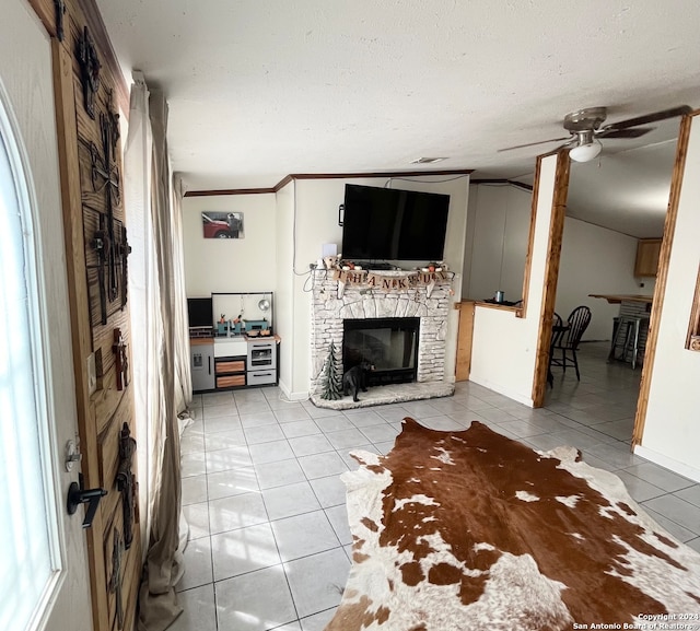 unfurnished living room featuring ceiling fan, ornamental molding, a textured ceiling, a fireplace, and light tile patterned flooring