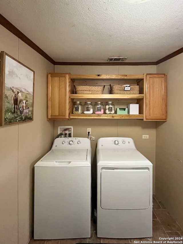 clothes washing area featuring crown molding, cabinets, a textured ceiling, and washing machine and dryer