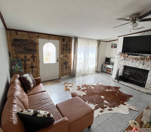 tiled living room with a textured ceiling, a stone fireplace, ceiling fan, and ornamental molding