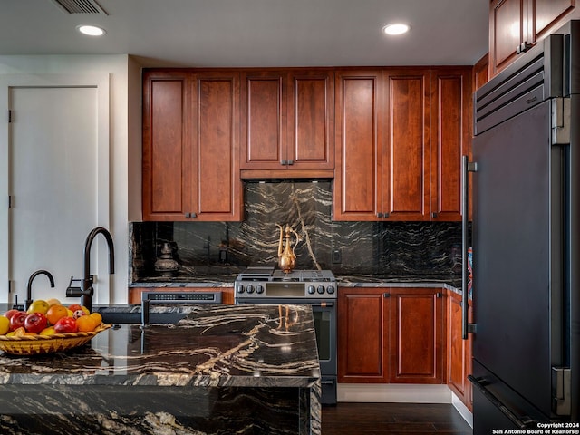 kitchen with dark wood-type flooring, appliances with stainless steel finishes, backsplash, and dark stone counters