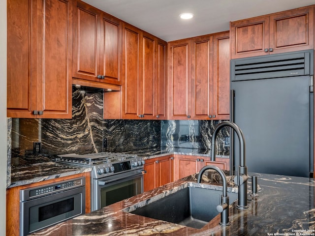 kitchen with dark stone countertops, backsplash, premium range hood, sink, and premium appliances