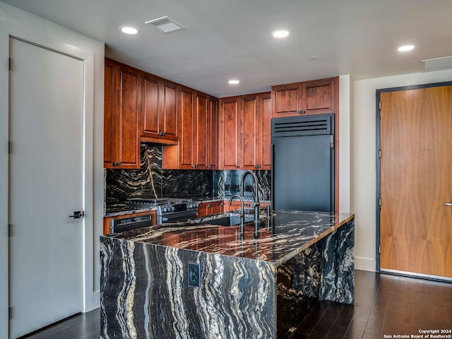 kitchen featuring dark stone countertops, high end appliances, sink, dark hardwood / wood-style floors, and decorative backsplash