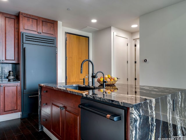 kitchen with dark stone counters, sink, dark wood-type flooring, appliances with stainless steel finishes, and a center island with sink