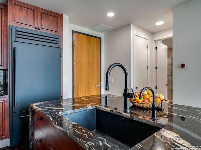 kitchen featuring dark stone countertops, stainless steel built in fridge, and sink