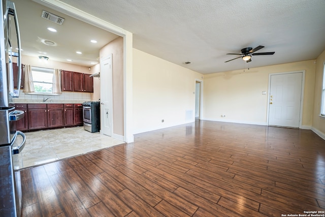 kitchen featuring light wood-type flooring, stainless steel gas stove, tasteful backsplash, sink, and ceiling fan