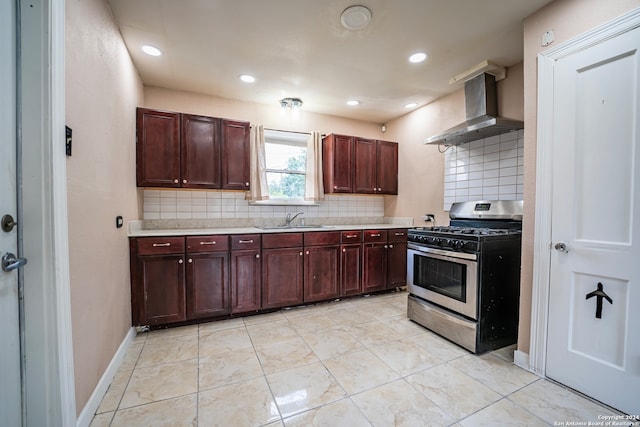 kitchen featuring gas range, wall chimney exhaust hood, backsplash, sink, and light tile patterned flooring