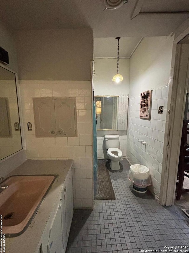 bathroom featuring vanity, toilet, tile patterned floors, a wainscoted wall, and tile walls