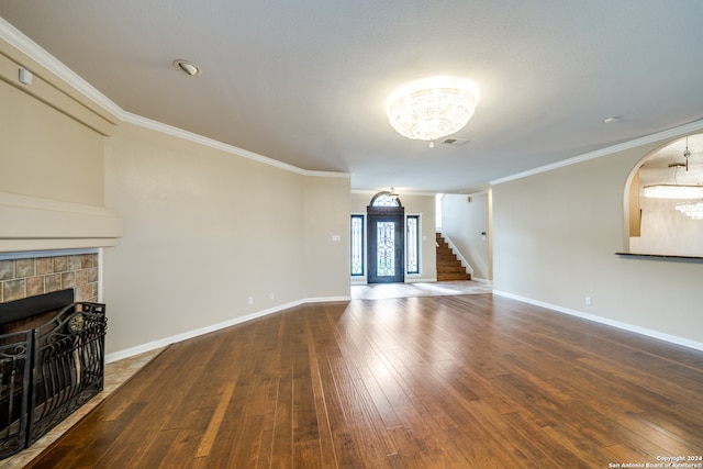 unfurnished living room featuring hardwood / wood-style flooring, a tiled fireplace, an inviting chandelier, and ornamental molding