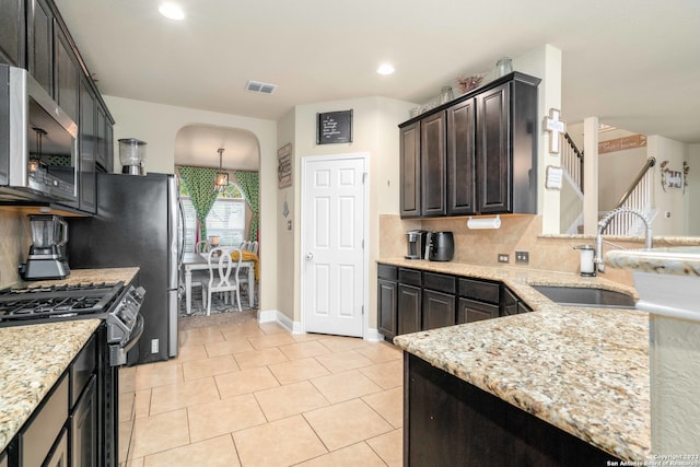 kitchen featuring appliances with stainless steel finishes, sink, light stone countertops, and dark brown cabinetry