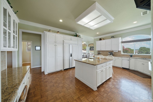 kitchen with a kitchen island, stone countertops, tasteful backsplash, ornamental molding, and white cabinetry