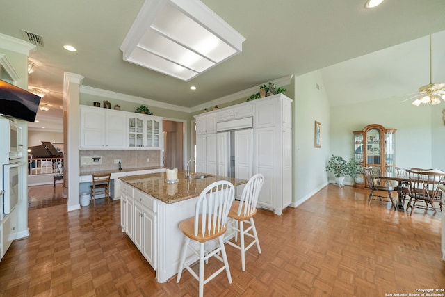 kitchen with white cabinets, stone counters, lofted ceiling, an island with sink, and ceiling fan