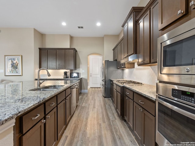 kitchen featuring appliances with stainless steel finishes, light hardwood / wood-style flooring, light stone counters, and sink