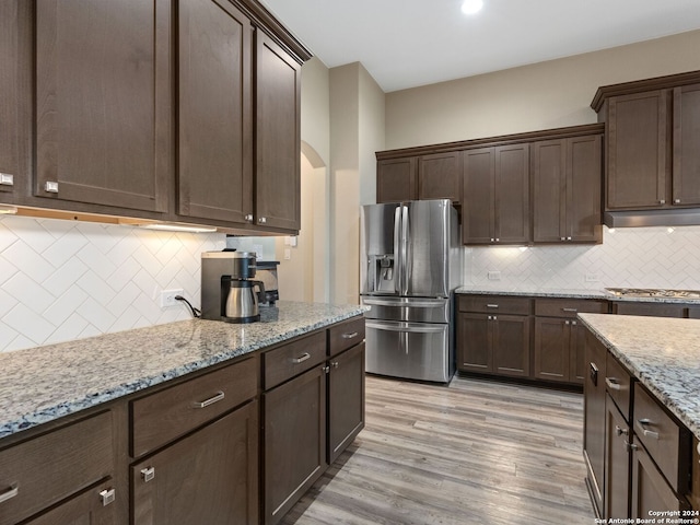 kitchen with dark brown cabinets, decorative backsplash, light stone countertops, stainless steel fridge with ice dispenser, and light hardwood / wood-style floors