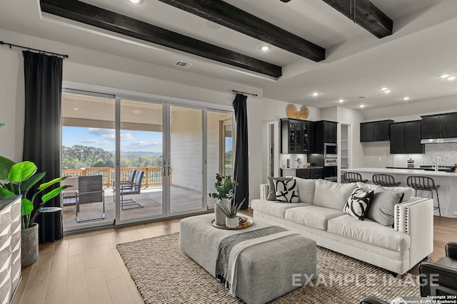 living room featuring light wood-type flooring, beamed ceiling, and sink