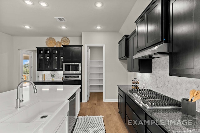 kitchen featuring backsplash, appliances with stainless steel finishes, sink, light wood-type flooring, and dark stone counters