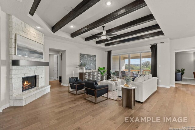 living room with light wood-type flooring, ceiling fan, and a stone fireplace