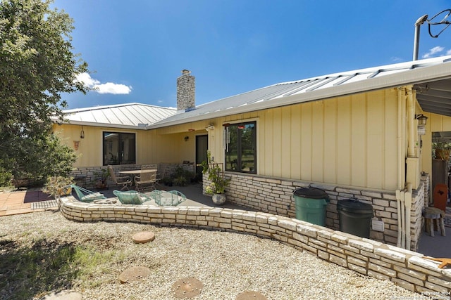 back of house with a standing seam roof, a patio, a chimney, and metal roof