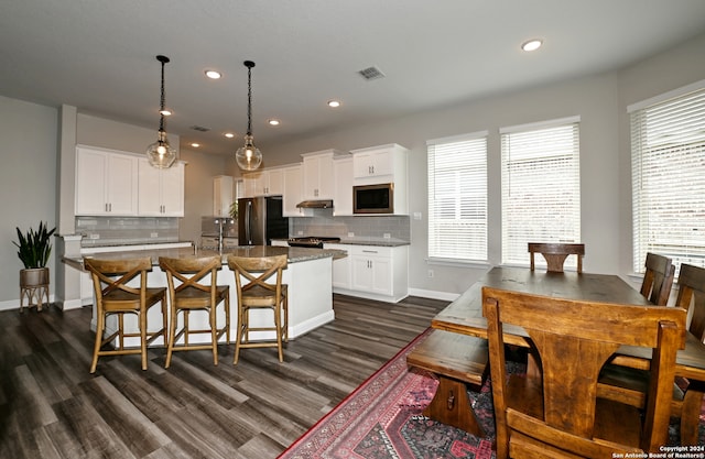 kitchen featuring dark wood-type flooring, stainless steel appliances, white cabinetry, and a kitchen island with sink