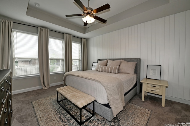 bedroom featuring multiple windows, a raised ceiling, dark colored carpet, and ceiling fan