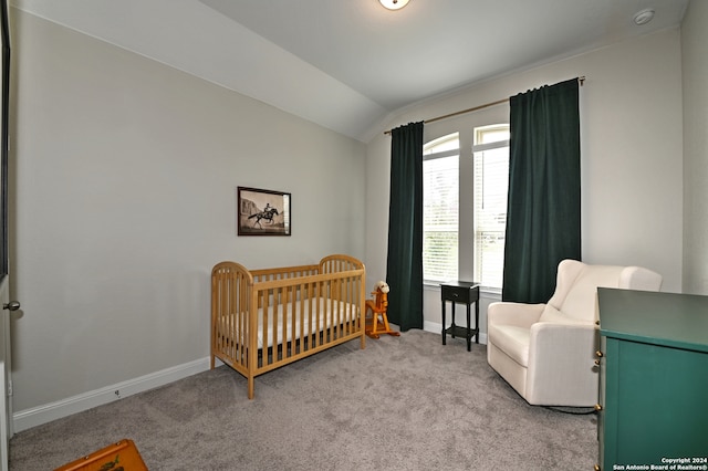 carpeted bedroom featuring a crib and lofted ceiling