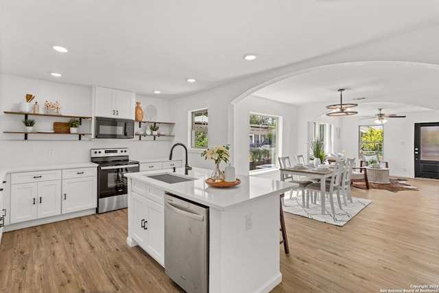 kitchen with arched walkways, stainless steel appliances, a sink, light wood-style floors, and open shelves