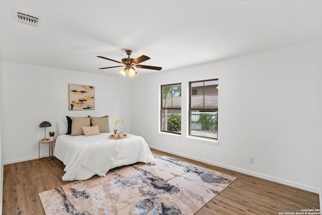 bedroom featuring visible vents, ceiling fan, baseboards, and wood finished floors