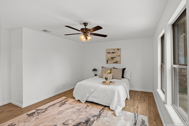 bedroom featuring a ceiling fan, wood finished floors, visible vents, and baseboards