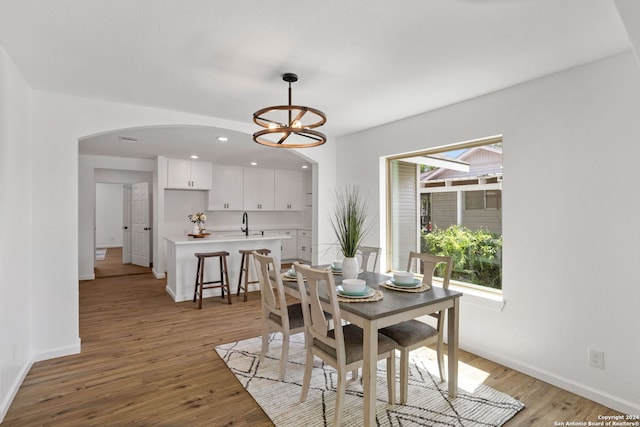 dining room with a wealth of natural light, a notable chandelier, sink, and light hardwood / wood-style floors