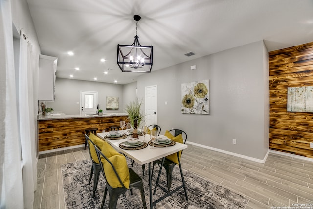 dining room featuring light wood-type flooring, wooden walls, and a chandelier