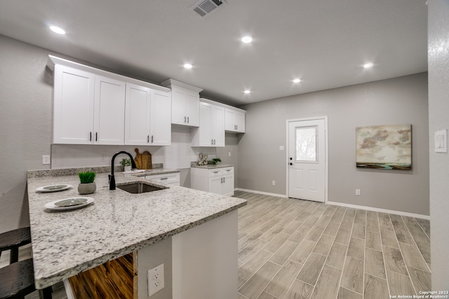 kitchen with a kitchen breakfast bar, light stone counters, kitchen peninsula, sink, and light hardwood / wood-style floors