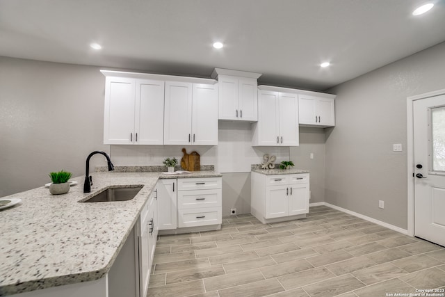 kitchen featuring kitchen peninsula, sink, light stone countertops, and white cabinetry