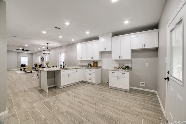 kitchen featuring light wood-type flooring, white cabinets, pendant lighting, and sink