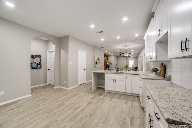 kitchen with light stone counters, white cabinetry, light hardwood / wood-style floors, and kitchen peninsula