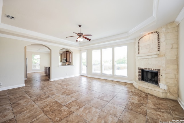 unfurnished living room featuring crown molding, ceiling fan with notable chandelier, a tray ceiling, and a fireplace