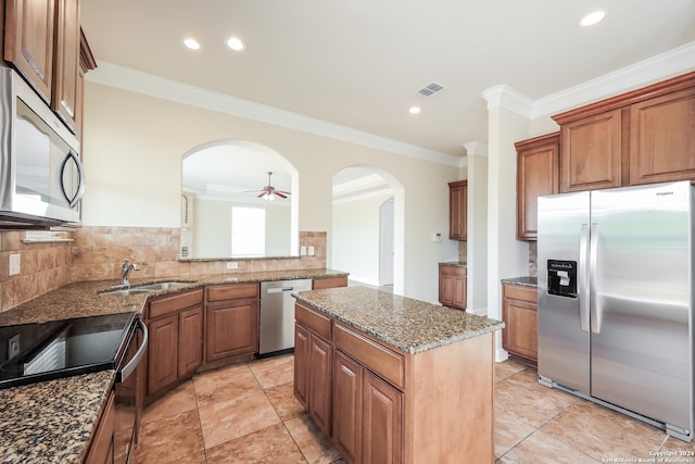 kitchen with ornamental molding, stainless steel appliances, a kitchen island, ceiling fan, and stone countertops