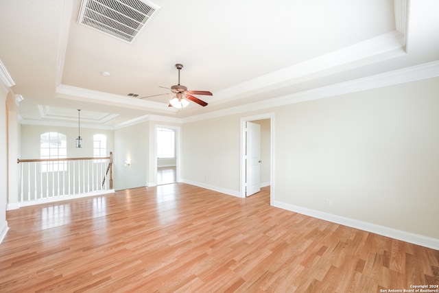 spare room with crown molding, a raised ceiling, ceiling fan with notable chandelier, and light hardwood / wood-style floors