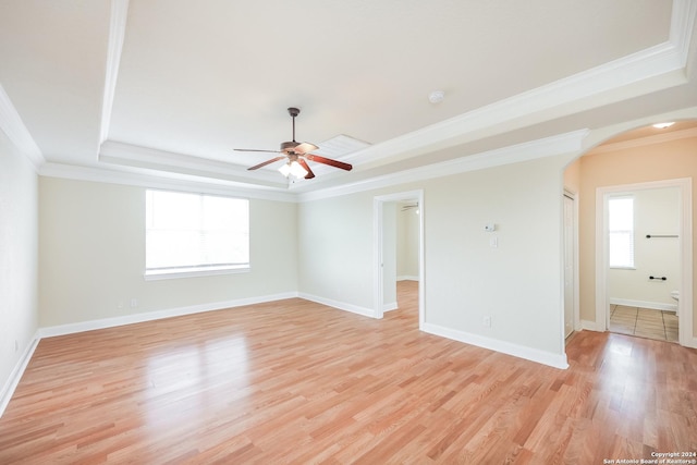 empty room with arched walkways, light wood finished floors, a tray ceiling, and ornamental molding