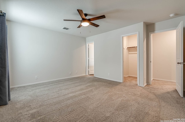 unfurnished bedroom with a closet, ceiling fan, a spacious closet, and light colored carpet