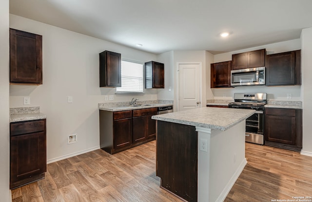 kitchen featuring light wood-type flooring, appliances with stainless steel finishes, sink, dark brown cabinets, and a kitchen island