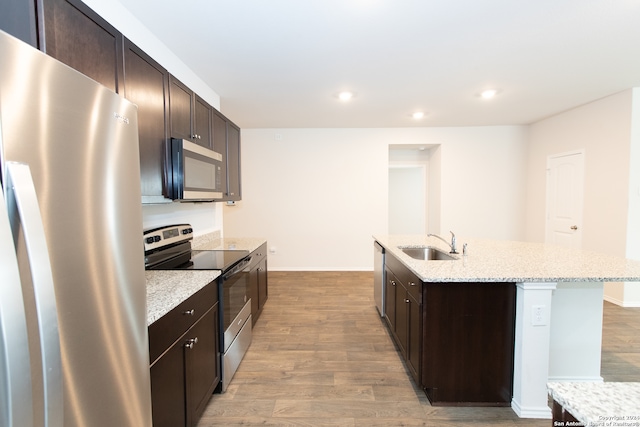 kitchen featuring stainless steel appliances, sink, light wood-type flooring, and a kitchen island with sink