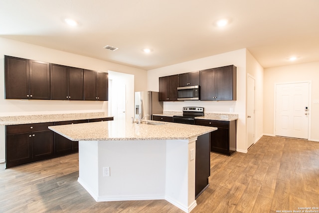 kitchen with a kitchen island with sink, light stone counters, appliances with stainless steel finishes, and light hardwood / wood-style floors