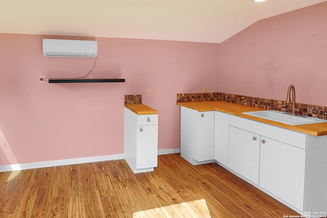 kitchen featuring a wall mounted air conditioner, light hardwood / wood-style flooring, sink, lofted ceiling, and white cabinets