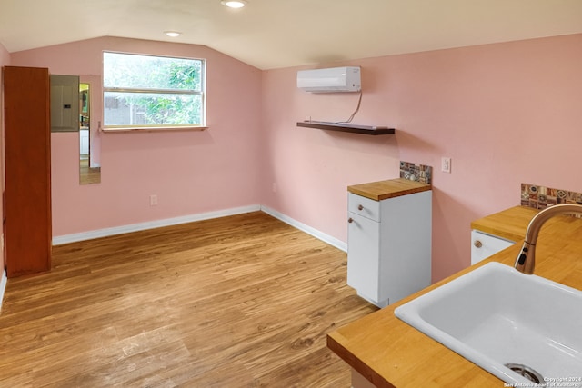 clothes washing area featuring electric panel, an AC wall unit, sink, and light hardwood / wood-style floors