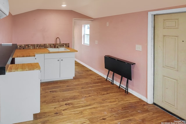 kitchen with vaulted ceiling, sink, white cabinetry, and light hardwood / wood-style floors