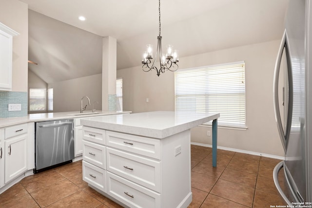 kitchen with lofted ceiling, appliances with stainless steel finishes, an inviting chandelier, and white cabinetry