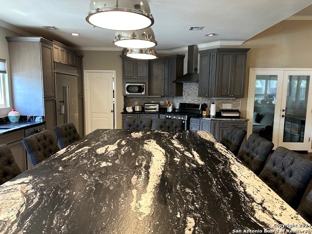 kitchen with wall chimney range hood, built in appliances, ornamental molding, and a breakfast bar