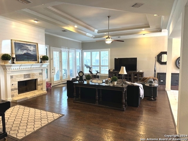 living room featuring a raised ceiling, dark hardwood / wood-style flooring, ceiling fan, and a stone fireplace