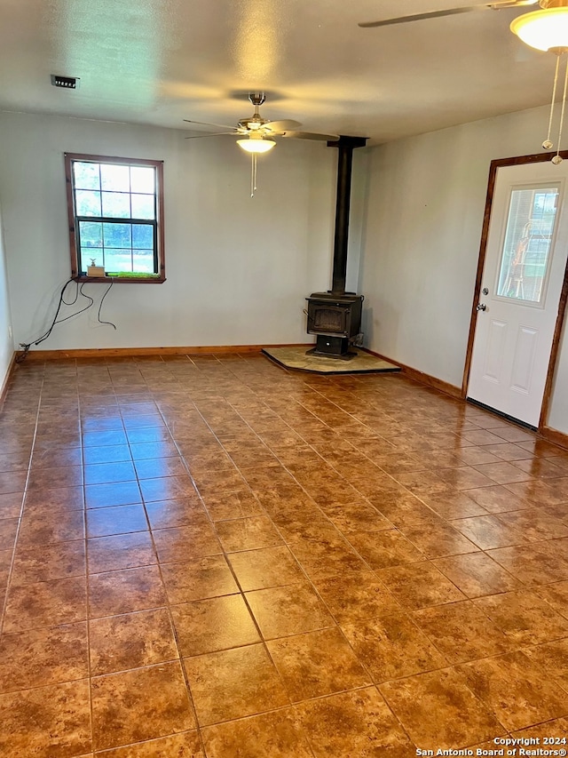 unfurnished living room with a wood stove, ceiling fan, and tile patterned flooring